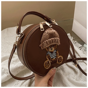 Detail der runden Handtasche mit Bärenstickerei und dekorativer brauner Strickmütze