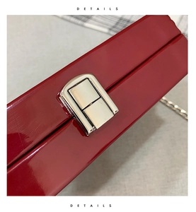 Close-up of sleek dark red glossy box bag with metallic clasp and chain detail