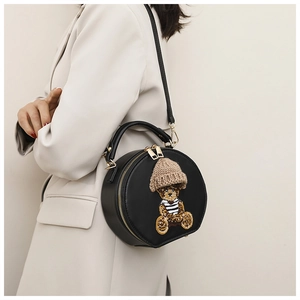 Detail einer runden schwarzen Handtasche mit Bären-Aufnäher getragen auf Beige