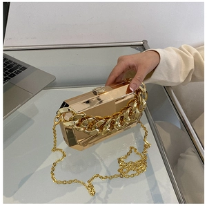 Detail of gold mirror finish acrylic box bag with chunky metal chain on glass table