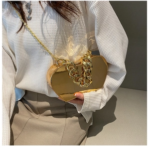 Close-up of golden heart-shaped hard shell clutch bag with metallic mirror finish and chains
