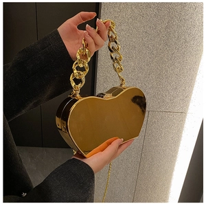 Detail of a gold heart-shaped metal clutch with mirror finish and chunky ring chain