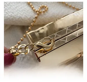 Macro detail of golden metal clasp and ball chain on a rhombus textured acrylic box bag