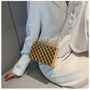 Detail of gold quilted metal box clutch bag with elegant bead chain on white blazer