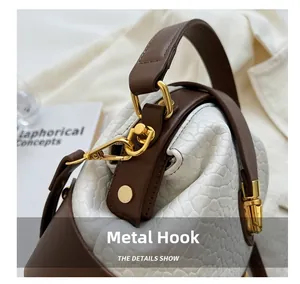 Detailed close-up of golden metal hooks and brown leather handle on a white textured bag