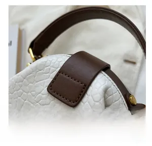 Close-up of white pebble leather texture with brown trim and polished gold hardware