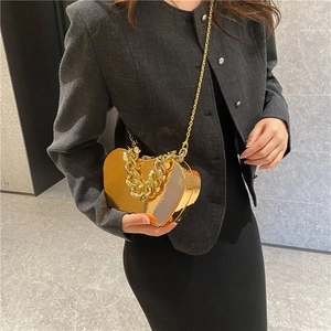 Luxury gold heart shaped metal clutch bag with chain strap shown on fashion model
