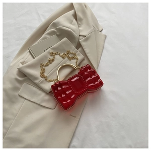 Détail de la pochette nœud rouge avec poignée dorée et chaîne sur une veste beige