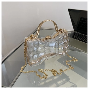 Détail d'une pochette transparente en forme de nœud avec chaîne et accessoires dorés
