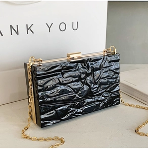 Close-up of black glossy crinkle-textured party clutch with gold metal frame and chain