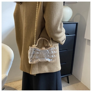 Détail d'une pochette nœud transparente avec chaîne dorée et fermoir perle en métal