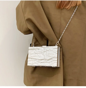 Detail of silver crackle textured handbag with sleek metal chain worn on a brown blazer