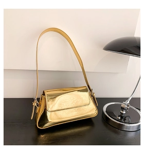 Macro detail of the golden metallic shoulder bag with mirror finish on a black wooden desk