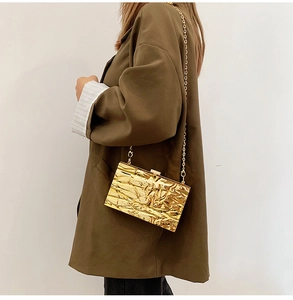 Close-up of golden textured box clutch with a fine metal chain on a brown blazer