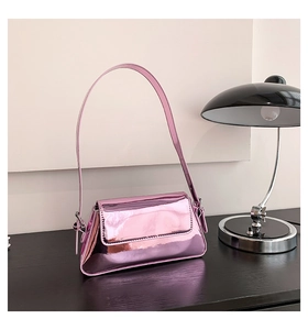 Detail of glossy pink metallic underarm bag showing mirror texture on a wooden desk