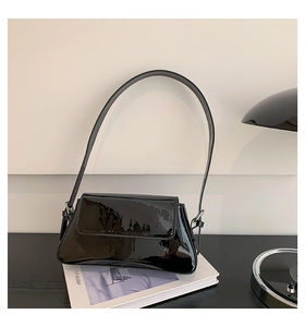 Close-up of black patent leather baguette shoulder bag with glossy finish and modern flap