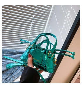 Close-up of a green glossy patent leather mini bag with gold text and metallic buckles