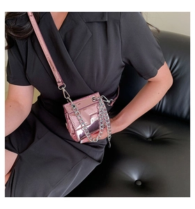 Détail du mini sac boîte rose métallisé avec chaîne argentée porté sur une robe noire