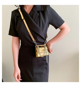 Gros plan d'un mini sac doré métallisé avec chaîne argentée sur robe noire