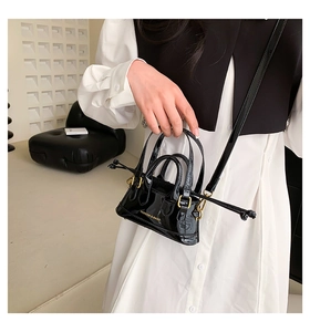 Close-up of black patent leather mini shell bag with gold logo and crossbody strap