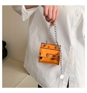Détail d'un mini sac orange verni brillant avec bandoulière chaîne argentée et texte mode