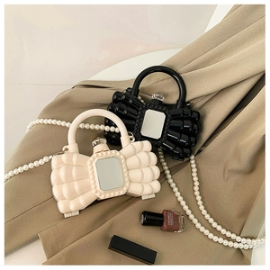 Dettaglio di pochette in acrilico a forma di fiocco con catene di perle bianche e nere