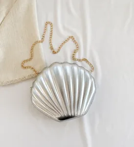 Detail showing the silver metallic shell-shaped crossbody bag with golden chain strap