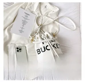 Detailed top view of white bucket bag with 'THE BUCKET' print and smartphone for size
