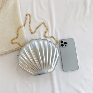 Silver shell-shaped crossbody bag size comparison with a smartphone and chain strap