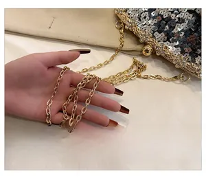 Detailed close-up of golden metal chain strap on sequined evening clutch with crystals