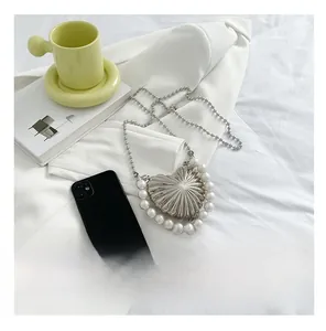 Mini heart-shaped silver metal bag with pearl trim compared to a smartphone