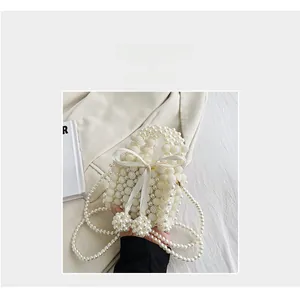 Detail of cream white pearl woven handbag with satin bow and crossbody chain strap