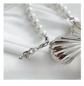 Detail of silver shell-shaped mini bag with pearl strap and polished metal hardware