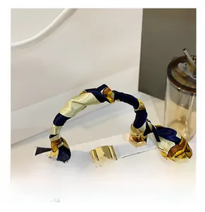 Detail showing the white textured bag with a silk scarf wrapped handle and gold buckle