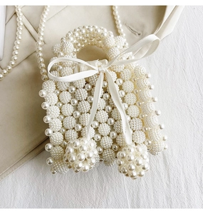 Detail of handmade cream pearl woven handbag featuring a white silk bow and long chain strap
