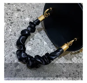 Close-up of black pleated handle with gold cylindrical metal hardware on evening bag