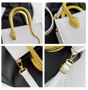 Detail of white crocodile pattern handbag featuring a gold snake-shaped metal handle