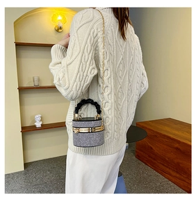 Close-up of sparkling rhinestone bucket bag with woven handle and metallic chain strap