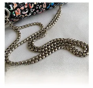 Detailed shot of silver metal square-link chain strap on black graffiti pattern PU bag