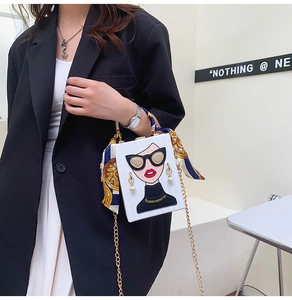 Detail of white box clutch bag featuring cartoon woman applique and silk scarf handle