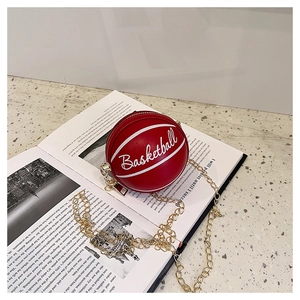 Detail of red mini basketball shaped crossbody bag with gold chain strap on an open book