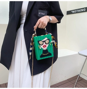 Detailed view of green box bag with cartoon icon, silk scarf handle and gold chain