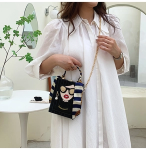 Detail of box bag with fashion girl illustration and scarf-wrapped handle on a gold chain