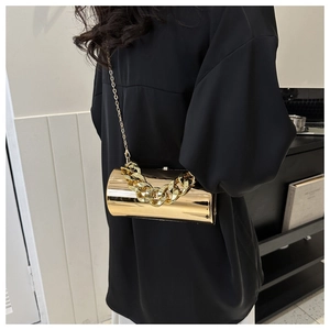 Detail of a cylindrical gold metal clutch with a chunky decorative chain and slim strap