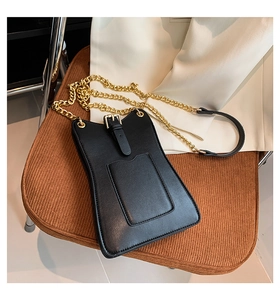 Détail d'un petit sac bandoulière en cuir noir avec chaîne dorée sur chaise en velours