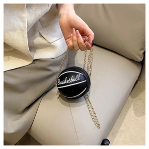 Detail of a basketball-shaped black chain bag held by hand in a minimalist setting