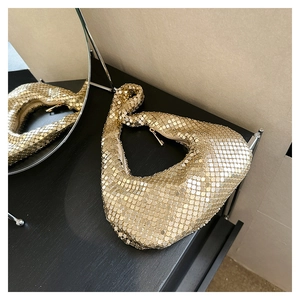 Détail du sac hobo à paillettes dorées avec reflet de miroir sur surface en bois noir