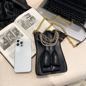Sac bandoulière créatif en cuir noir forme torse avec chaîne dorée sur bureau blanc moderne