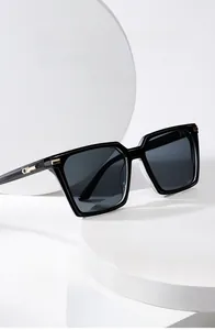 Detail of square black frame sunglasses with golden metal accents on a white tray
