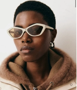 Detail of angular cat-eye sunglasses with cream frame and brown lenses on a model